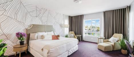Habitación de hotel con una cama grande, una silla, una mesita y vistas al exterior.