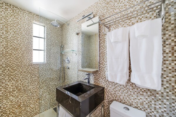Un baño con pared de mosaicos de azulejos, un lavamanos negro, un espejo y un perchero con dos toallas blancas.