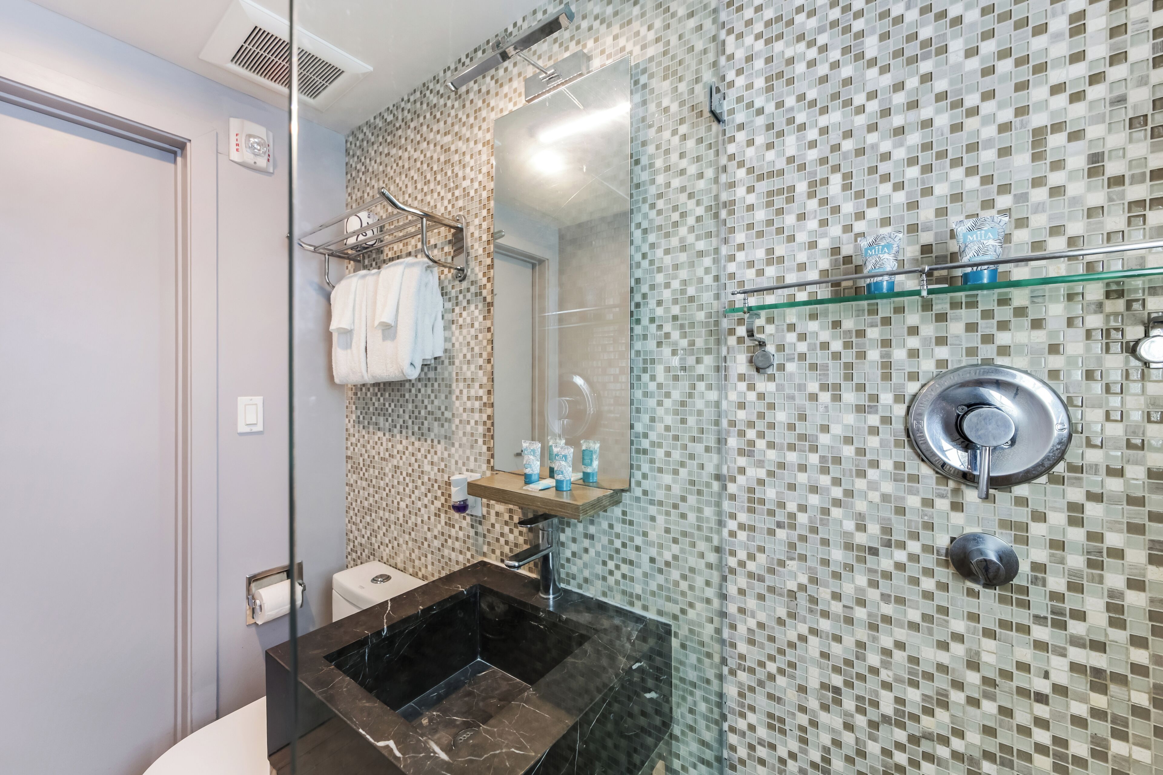 A modern bathroom with a glass shower enclosure, a black marble sink, and a tiled mosaic wall.