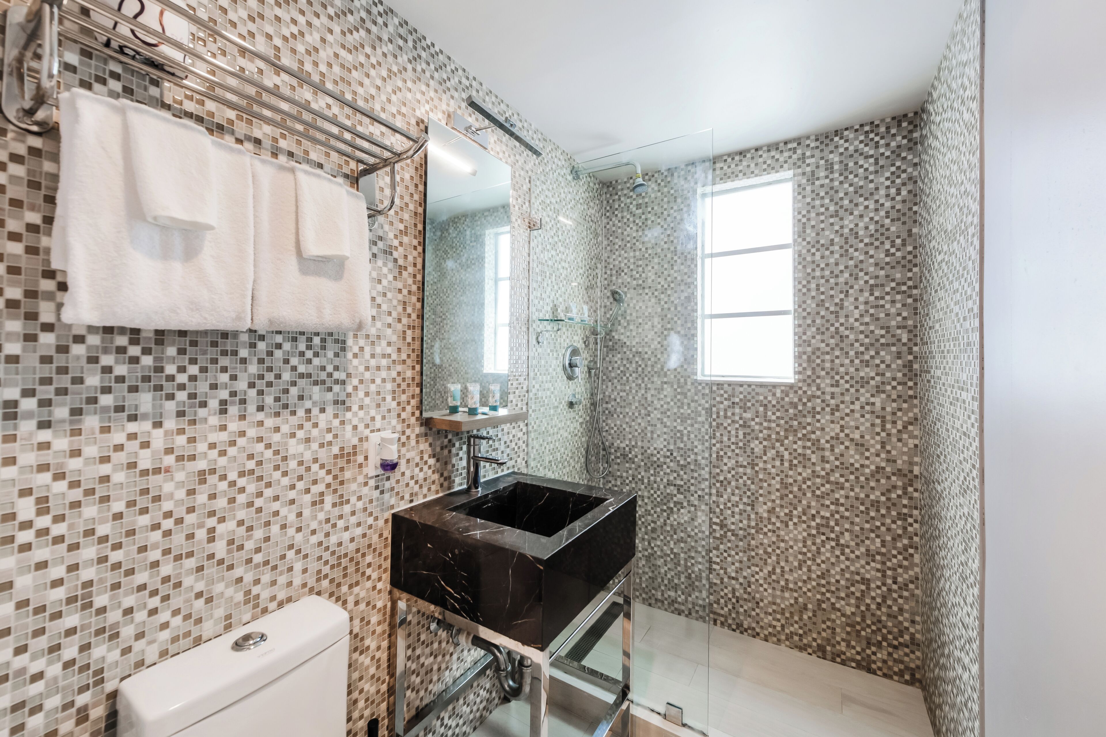 A bathroom with a tiled mosaic wall, a black sink, a glass shower enclosure, and a window.