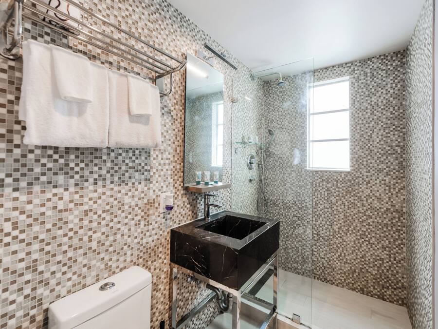 A bathroom with a tiled mosaic wall, a black sink, a glass shower enclosure, and a window.