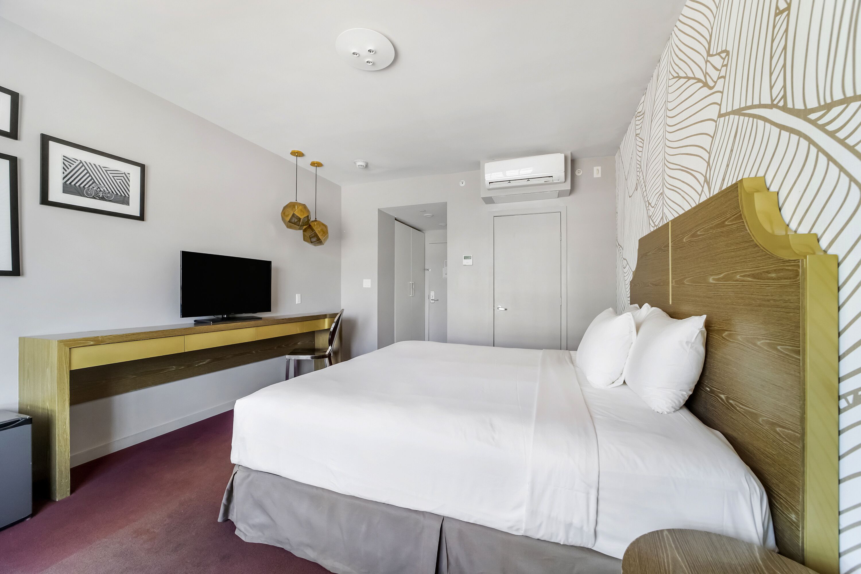 Una habitación de hotel con cama, escritorio, televisor y aire acondicionado.