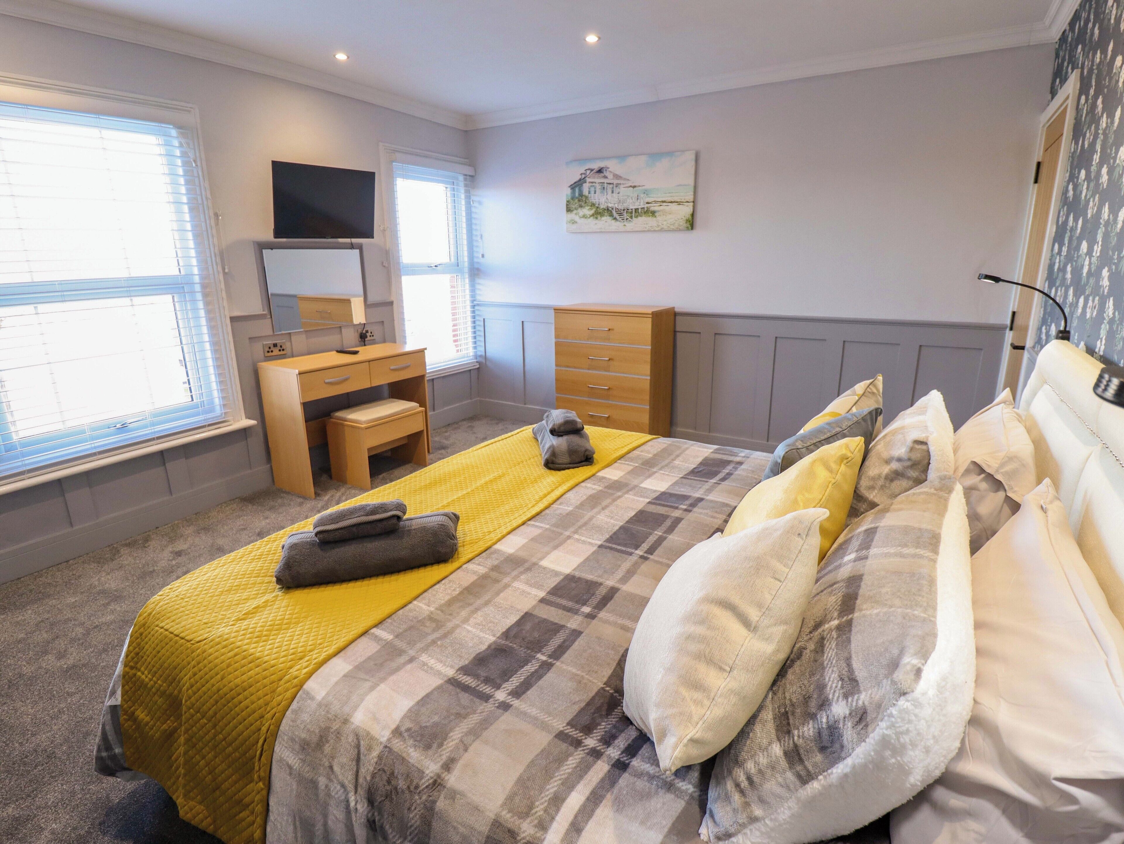 Une chambre à coucher avec un lit, un bureau, une commode, un téléviseur et un tableau accroché au mur.