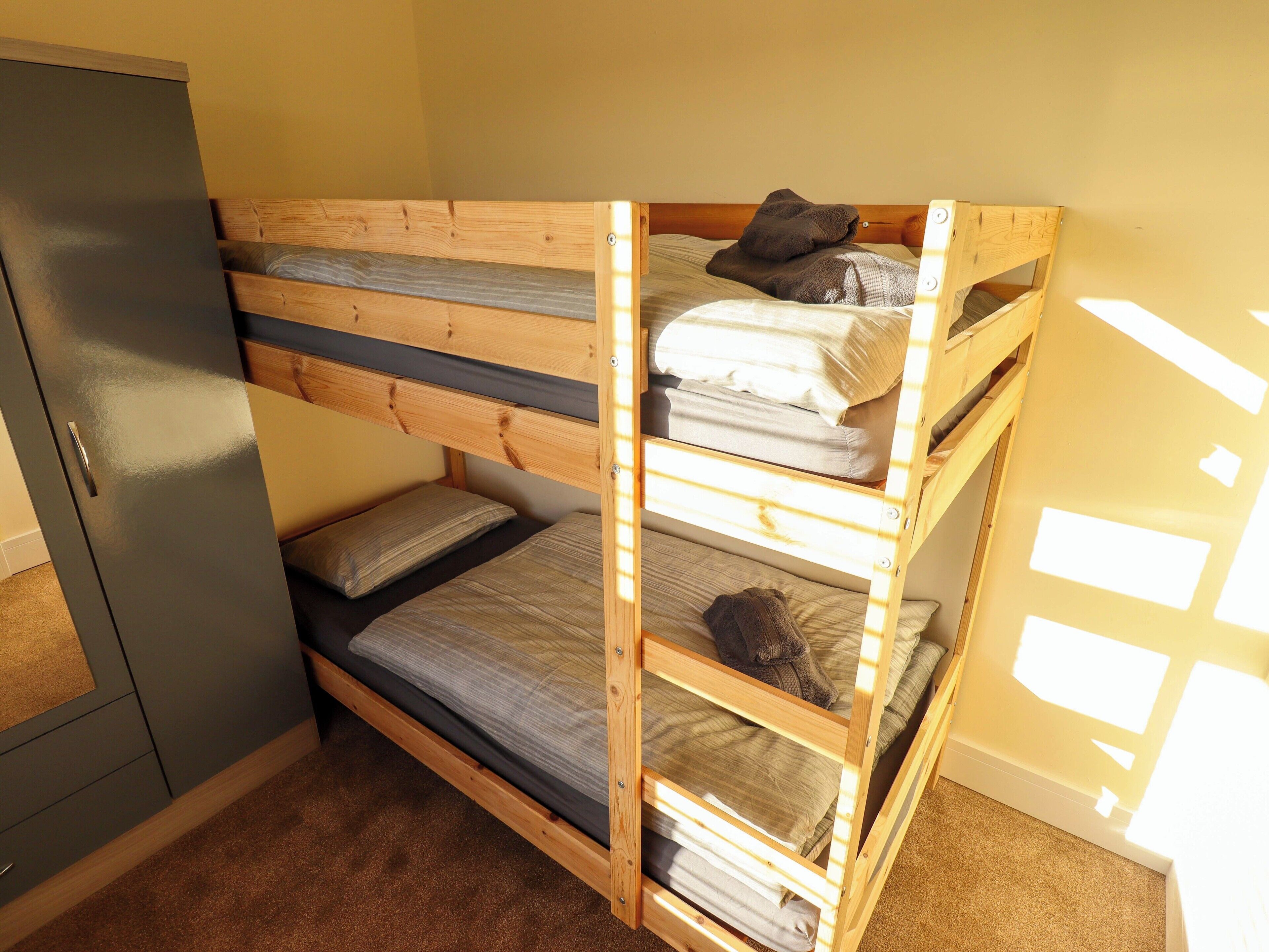 A bunk bed with a wooden frame, a grey cabinet, and a carpeted floor.