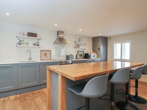 A modern kitchen with grey cabinets, a wooden island, bar stools, and a built-in oven. - Flat 6 (Tetbury)
