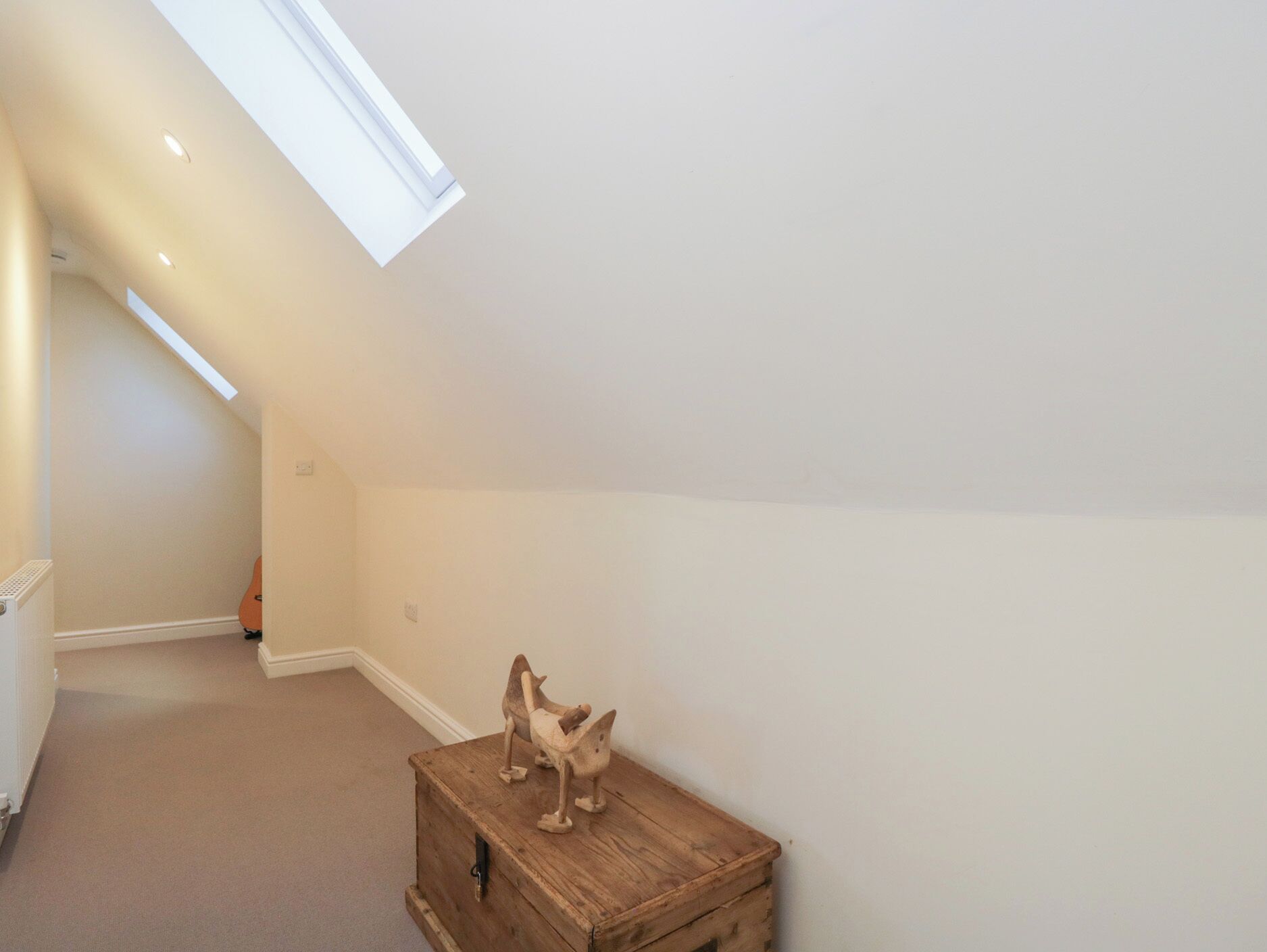 A room with a sloped ceiling, a skylight, and a wooden chest with two figurines.