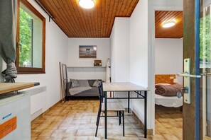 Une petite pièce comprenant un lit, une petite table, un radiateur et une fenêtre donnant sur des arbres.