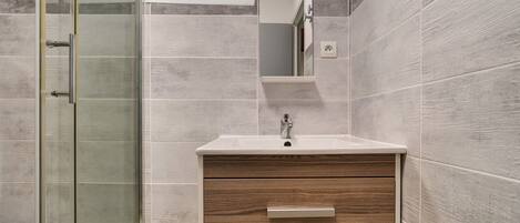 A bathroom with a glass shower enclosure, a wooden vanity with a sink, and a mirror.