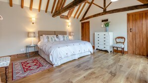 Un dormitorio con techo de madera, una cama con ropa de cama floral, un aparador, una silla y una alfombra.