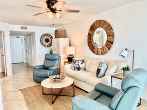 A living room with a ceiling fan, a round mirror, a sofa, a coffee table, and a chair.