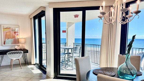 A balcony with a view of the sea, a dining table with chairs, a vase, and a lamp.