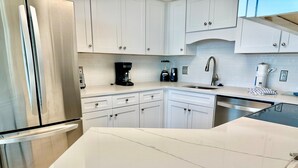 A modern kitchen with white cabinets, a stainless steel refrigerator, a coffee maker, and a dishwasher.