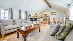 Een ruime woonkamer met een bank, een salontafel en een eethoek met stoelen. In de achtergrond is een keuken zichtbaar.