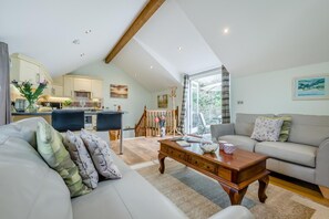 A spacious living room with a sofa, coffee table, and a view of the kitchen and balcony. - 2 Bed in Woodford (oc-a32063) (Woodford)