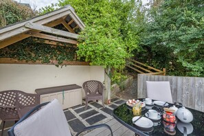 An outdoor patio with a table set for dining, surrounded by chairs and a bench. - 1 Bed in Woodford (oc-a32065) (Woodford)