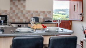 A kitchen with a view of the countryside, a dining area with chairs, and a breakfast setting. - 1 Bed in Woodford (oc-o32064) (Woodford)