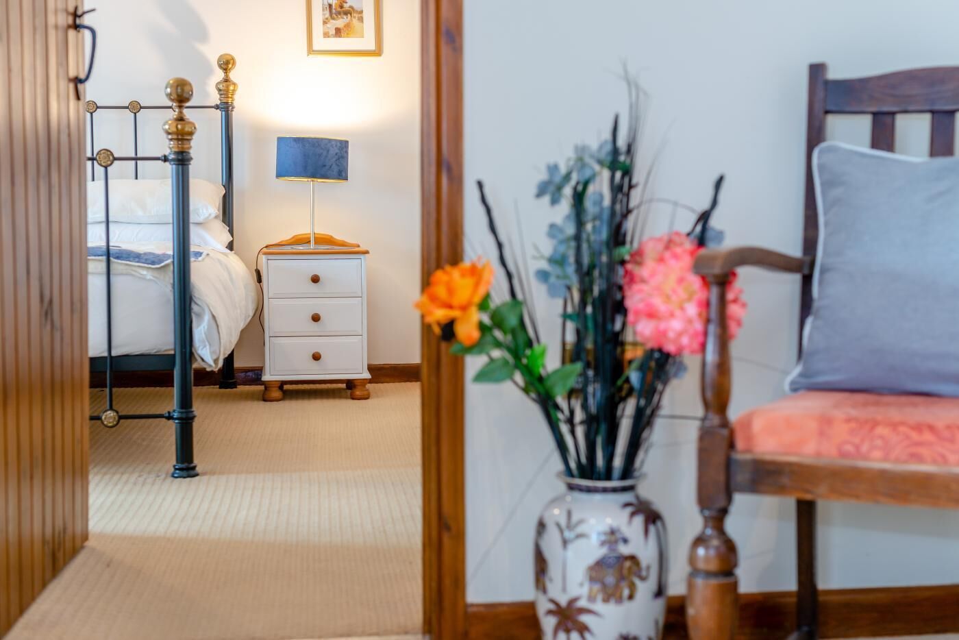 Ein Schlafzimmer mit Bett, Nachttisch, Lampe und einem Sessel mit Kissen.