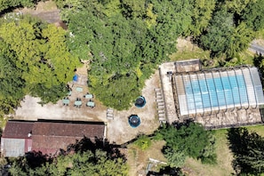 Eine Vogelperspektive zeigt ein Anwesen mit Schwimmbad, überdachter Außenlounge und einem Gebäude mit geneigtem Dach.