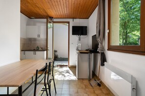 Une cuisine de taille réduite avec un plafond en bois, un téléviseur fixé au mur et une fenêtre donnant sur les arbres.