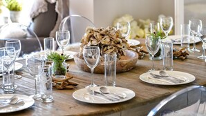 Mesa de jantar de madeira posta com pratos, talheres e copos de vinho, com um centro de mesa de ostras.