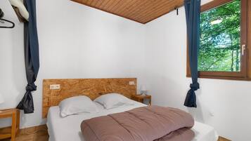 Ein Schlafzimmer mit hölzernem Kopfteil, einem Bett mit pinker Decke, einem Nachttisch mit Lampe und einem Fenster mit Vorhängen.