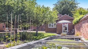 Un jardín con camas elevadas, una casa de ladrillo y un patio con mobiliario exterior.