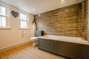Een moderne badkamer met een houten vloer, een ruime badkuip en een toilet.