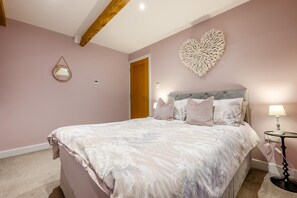 Een slaapkamer met een groot bed, een hartvormige decoratie aan de muur, een bedlamp en een houten balk in het plafond.