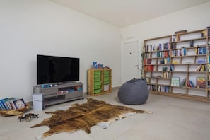 Ein Wohnzimmer mit Fernseher, Bücherregal und einer großen Tierfell-Decke auf dem Boden.