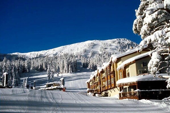 A snow-covered mountain with a ski resort building featuring multiple balconies and a ski lift in the background.