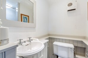 A bathroom with a white sink, two faucets, a mirror, a toilet, and a wall-mounted heater.