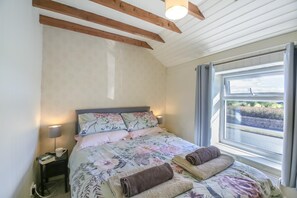 A bedroom with a bed, pillows, a nightstand, a lamp, and a window with a view.