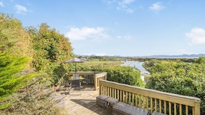 A wooden deck with outdoor furniture, a table, and an umbrella, overlooking a river and distant hills. - 2 Bed in Pwllheli (oc-s32070) (Pwllheli)