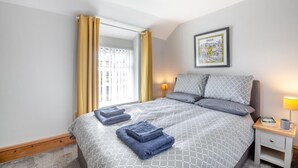 A neatly made bed with patterned bedding, a bedside table with a lamp, and a framed picture on the wall. - 2 Bed in Pwllheli (oc-s32070) (Pwllheli)