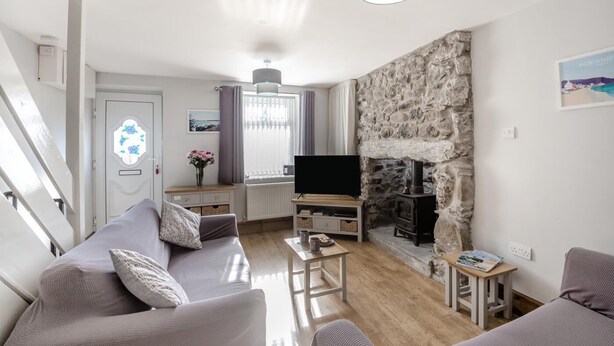 A modern living room with a stone fireplace, a sofa set, a television, and a small table with a vase of flowers. - 2 Bed in Pwllheli (oc-s32070) (Pwllheli)