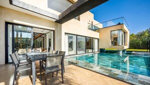Ein modernes Haus mit einem überdachten Pool, Sitzgelegenheiten im Freien und freiem Blick auf die umliegende Natur.