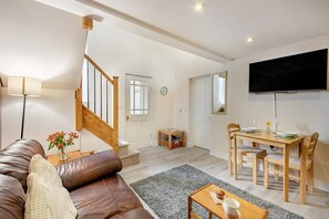 A spacious living room with a brown leather sofa, a wooden dining table with chairs, a staircase, and a flat-screen TV mounted on the wall. - 1 Bed in Berwick-upon-Tweed (oc-a32026) (Kyloe)