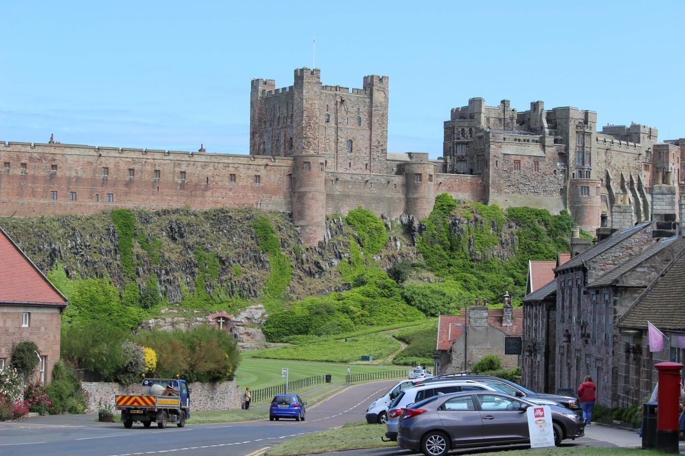 A castle on a hill with a road in the foreground and a truck parked on the side.