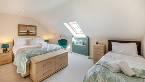A bedroom with two beds, a skylight, a painting on the wall, and a bedside table with a lamp.