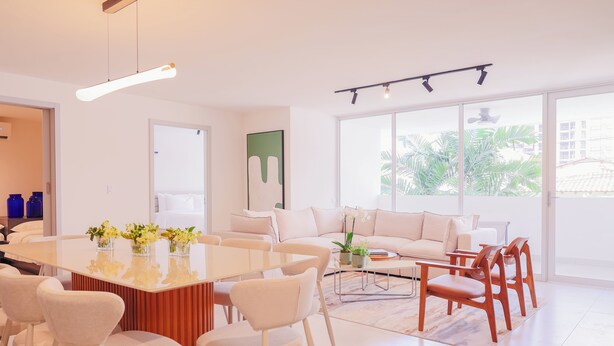 A modern living room with a central dining table, white sofas, and wooden chairs. - Edificio Doña Raquel (Panama City)