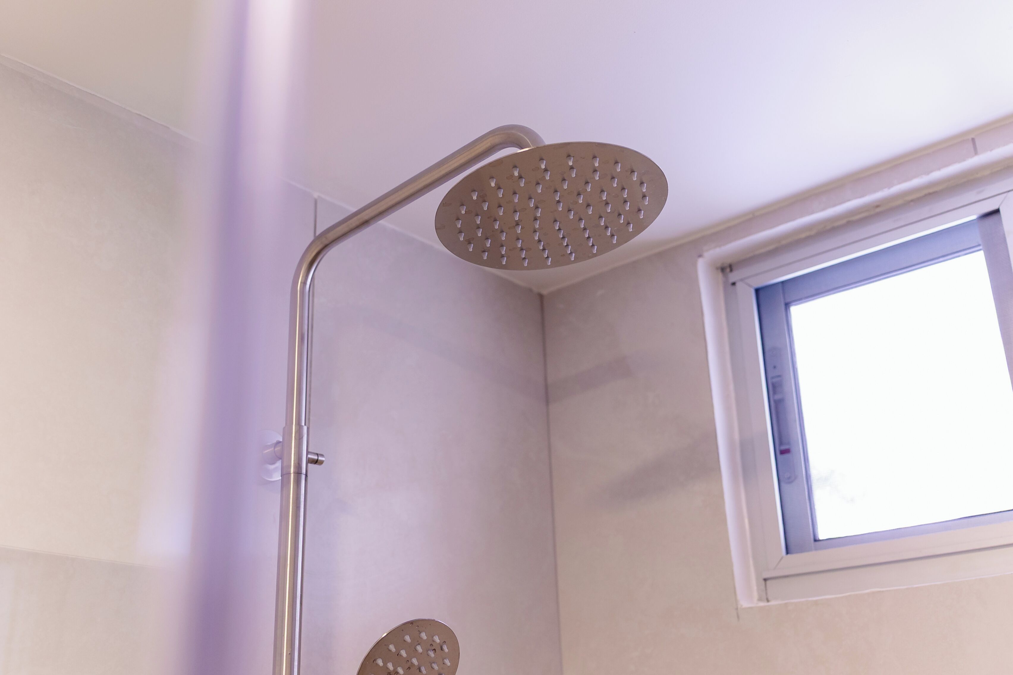 A shower with a handheld showerhead and a fixed showerhead in a corner of a room with a window.