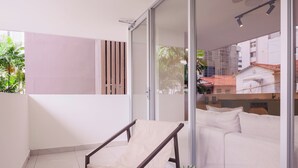 A balcony with a cushioned chair, a small table with a potted plant, and a glass door leading to an interior space with a sofa and a tiled floor. - Edificio Doña Raquel (Panama City)