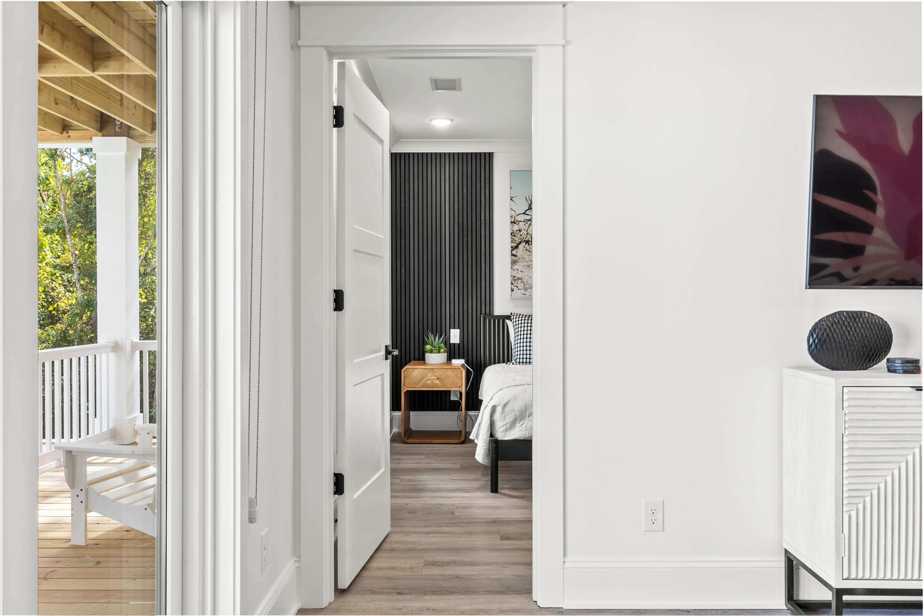 A room with a bed, a bedside table, a nightstand, a window with curtains, a wall-mounted artwork, and a white wardrobe.