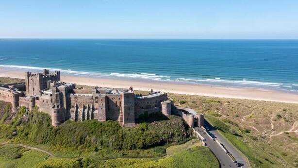 Een historisch kasteel met meerdere torens en muren, gelegen op een heuvel met uitzicht op een strand en de oceaan.