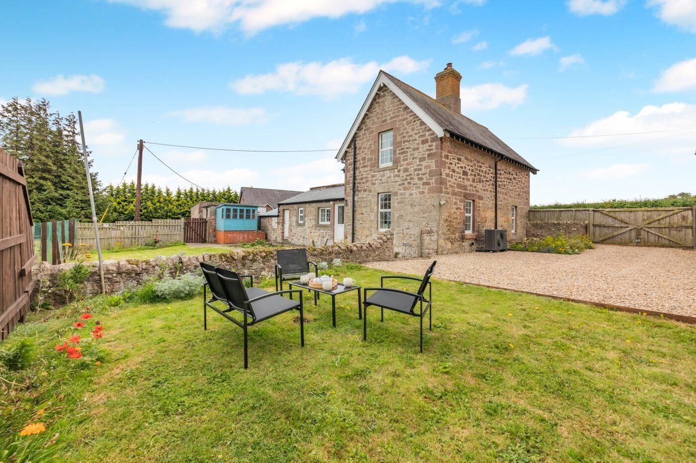 A stone house with a gravel driveway and a grassy backyard with outdoor seating.