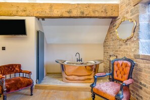 A room with a bathtub, two vintage chairs, a television, and a stone wall. - 7 Bed in Stoke-on-Trent (oc-t32196) (Stoke-on-Trent)
