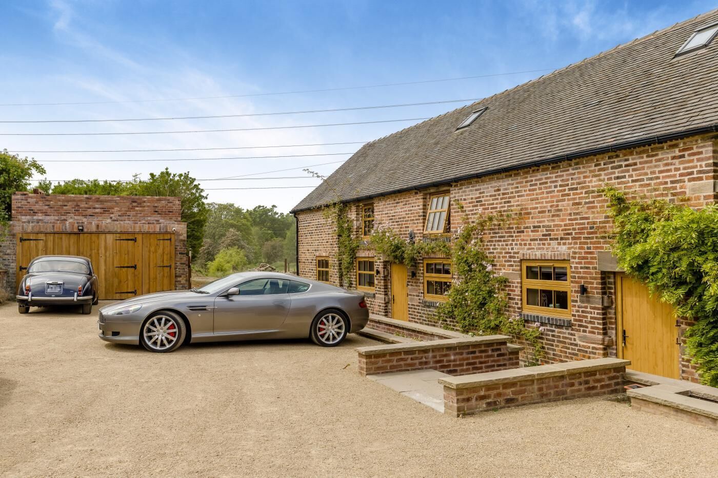Ein Backsteinhaus mit Carport, einem Oldtimer und einem modernen Sportwagen vor der Fassade.