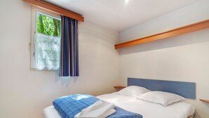 Ein Bett mit blauer und weißer Bettdecke, einem Holzkopfende und einem Fenster mit Vorhang.