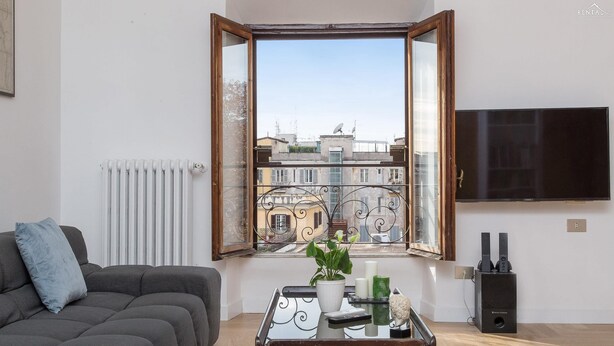Ein Wohnzimmer mit einer Couch, einem Couchtisch mit Dekoration, einem Fernseher und einem Fenster mit freiem Blick auf Gebäude.