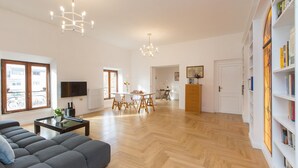 Ein geräumiges Wohnzimmer mit einer Couch, einem Essbereich mit Tisch und Stühlen, einem Bücherregal und einem an der Wand befestigten Fernseher.